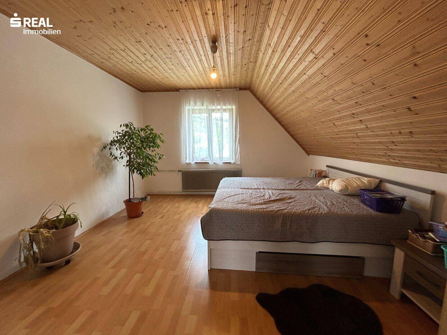 Geräumiges Schlafzimmer im Dachgeschoss mit Holzdecken, Doppelbett und Fenster.