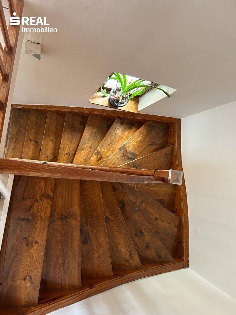 Holztreppe führt in die obere Etage, mit einem kleinen Fenster für natürliches Licht.