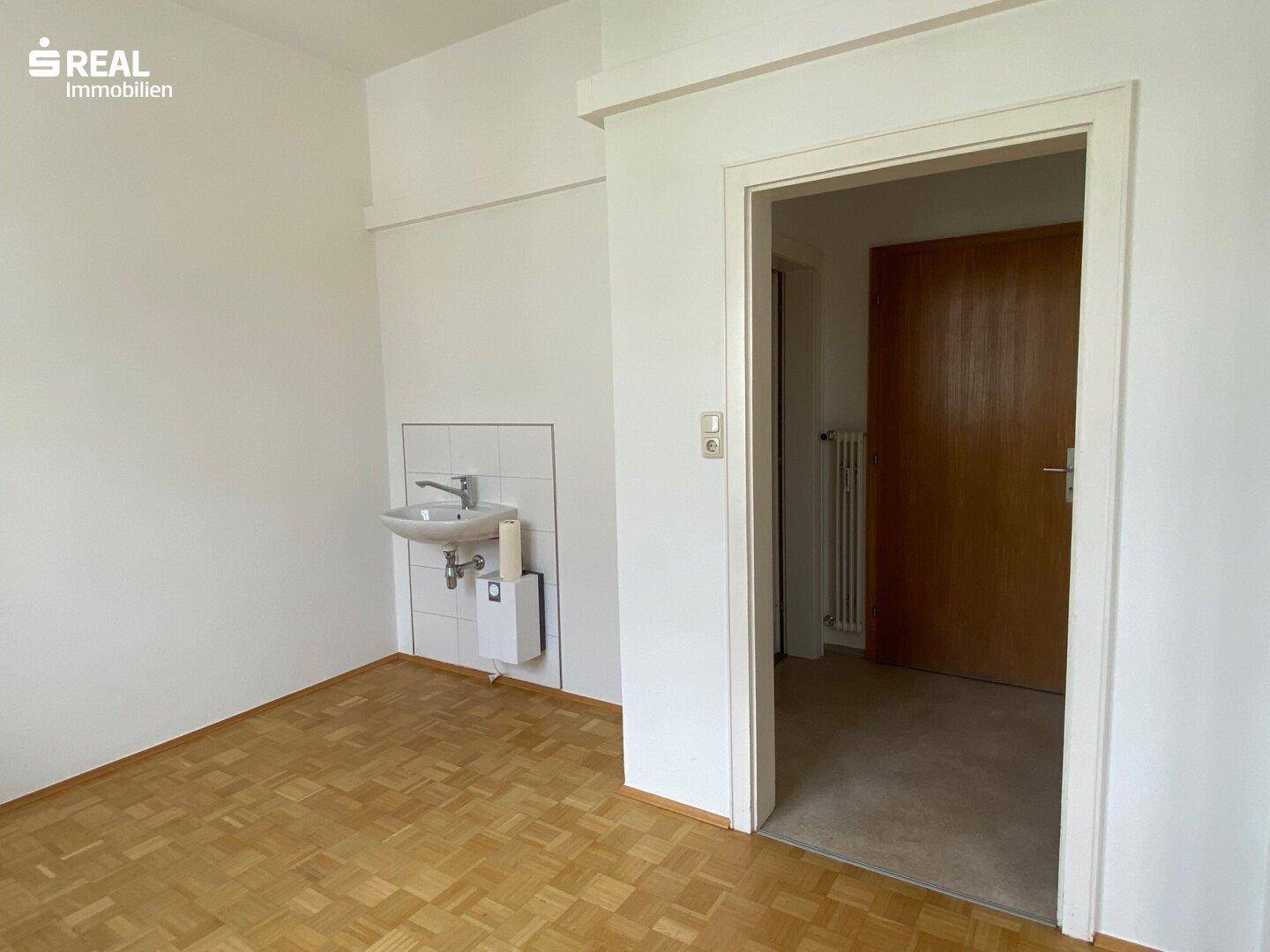 Büroraum mit integriertem Waschbecken und Parkettboden, ideal für vielseitige Nutzungsmöglichkeiten.