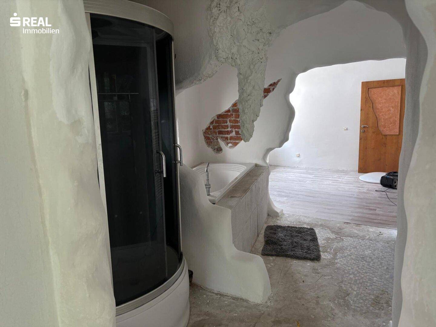Unkonventionelles Badezimmer mit Dusche und Badewanne, umgeben von skulpturalen Wänden.