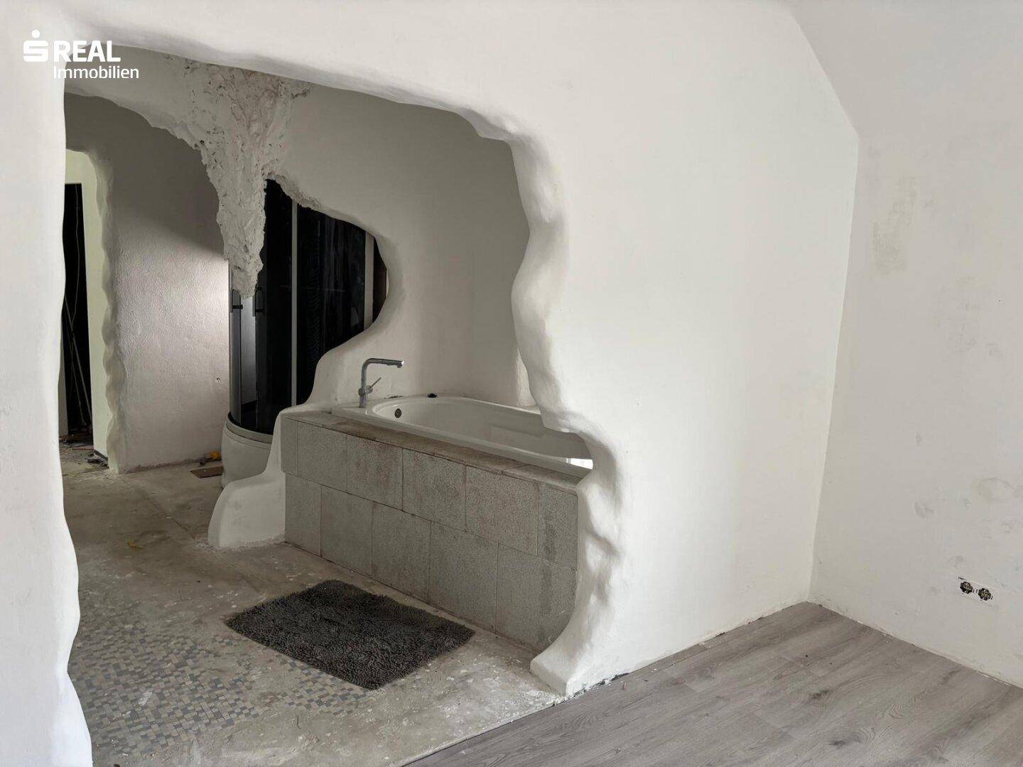 Badezimmer mit eingebauter Badewanne und künstlerisch gestalteten, organischen Wandstrukturen.