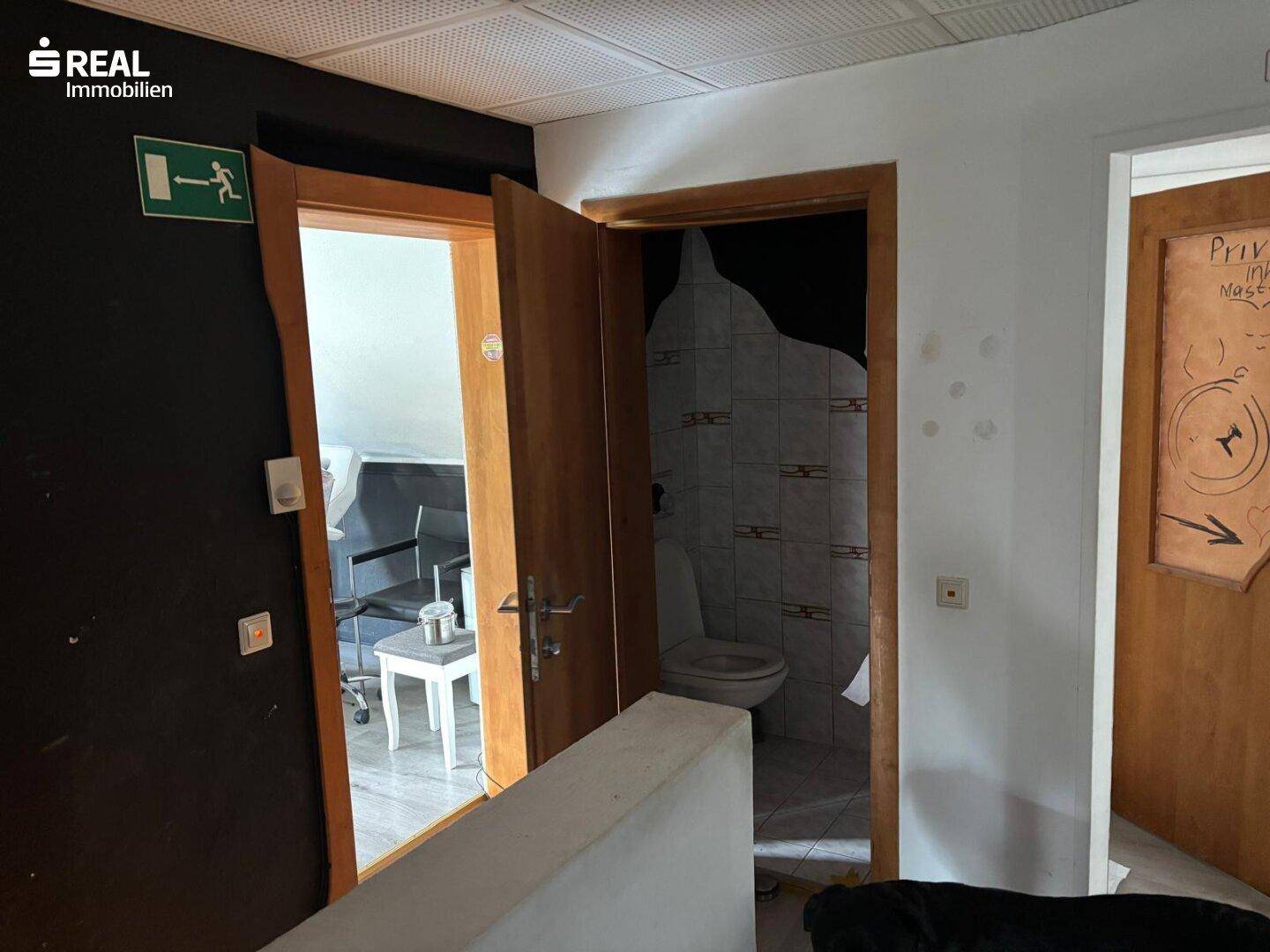 Kleines WC mit Fliesen und einer Holztür, angrenzend an einen weiteren Raum.