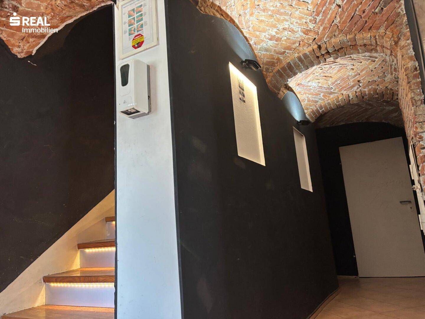 Historischer Treppenaufgang mit freigelegten Ziegelgewölben und modernen LED-Stufenbeleuchtung.