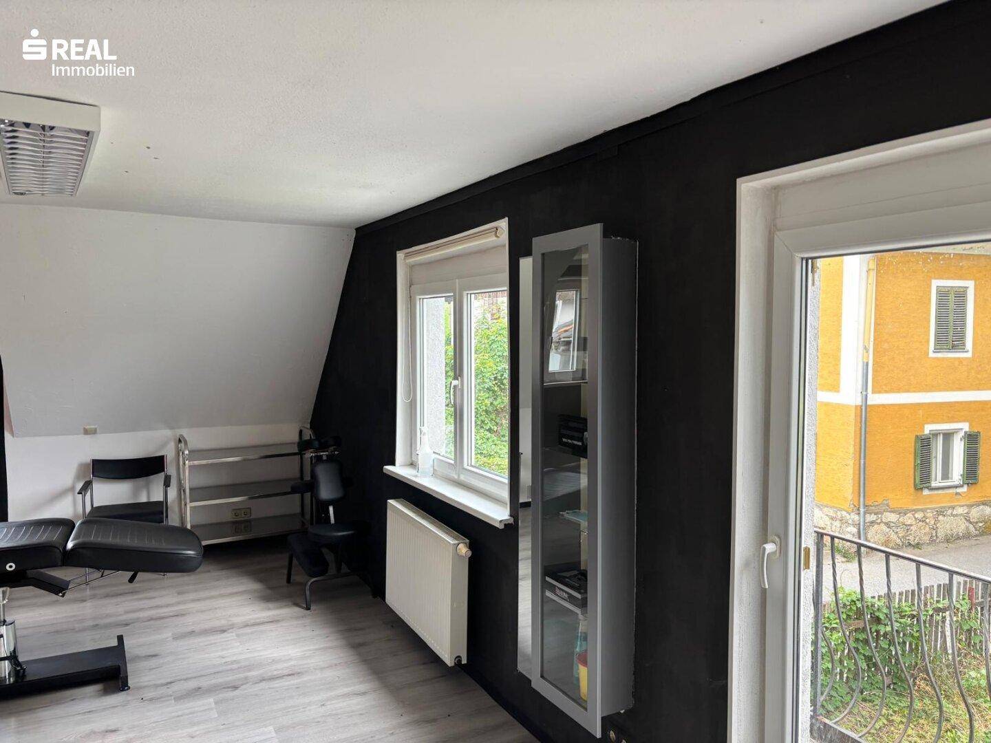 Dachgeschosszimmer mit schrägen Wänden, Laminatboden und Zugang zu einem französischen Balkon.