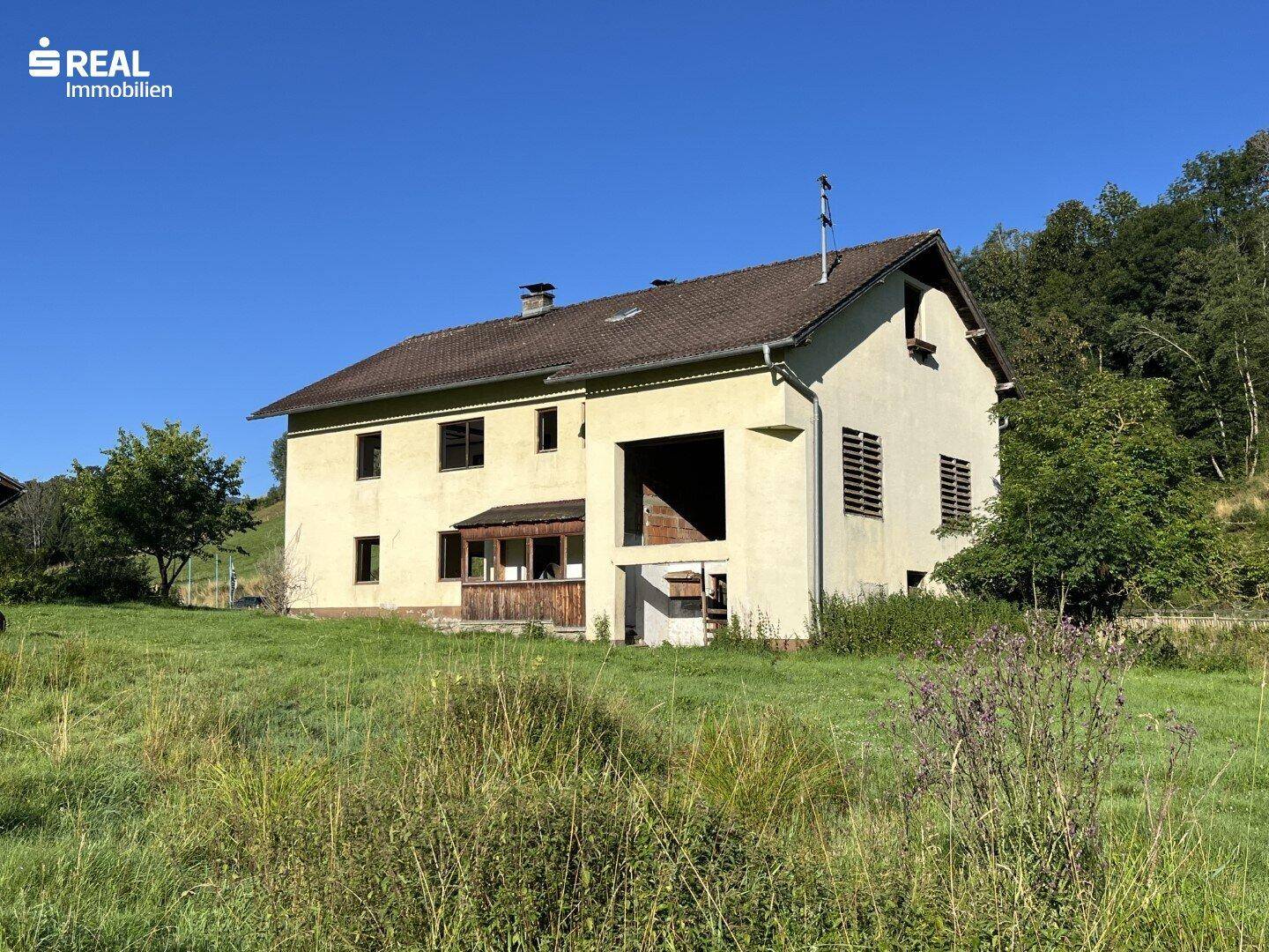 Ansicht des Landhauses von der Seite mit einfacher Architektur und weitem Blick ins Grüne.
