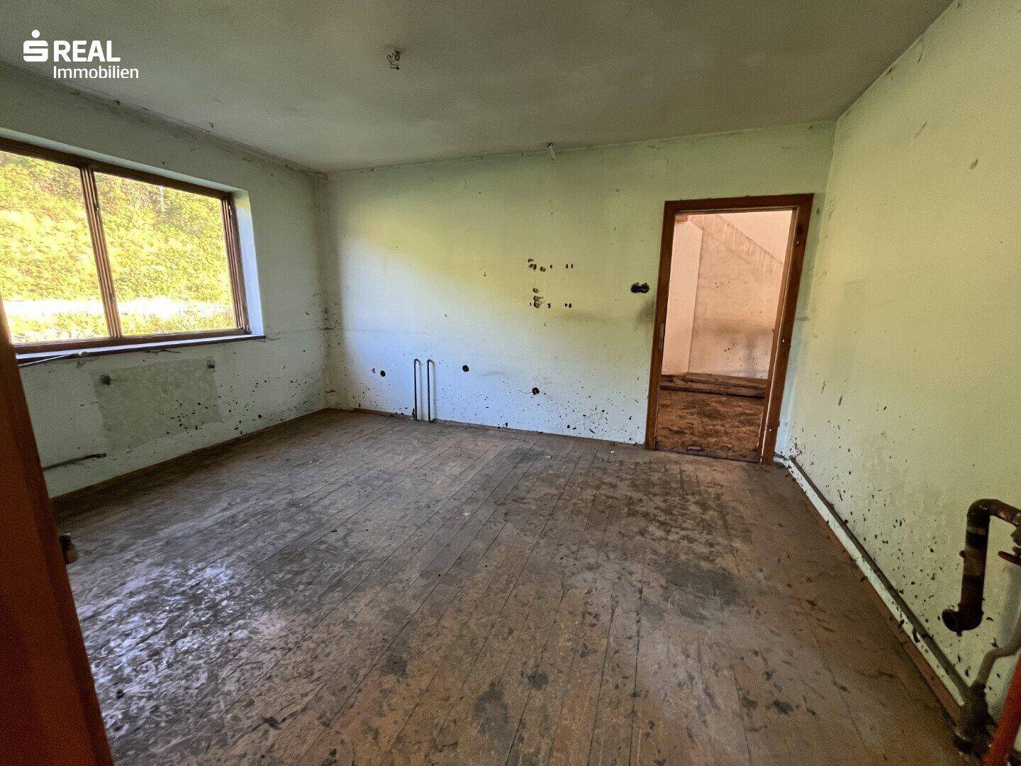 Leerer Raum mit abgenutztem Holzboden, grünen Wänden und einem Fenster.