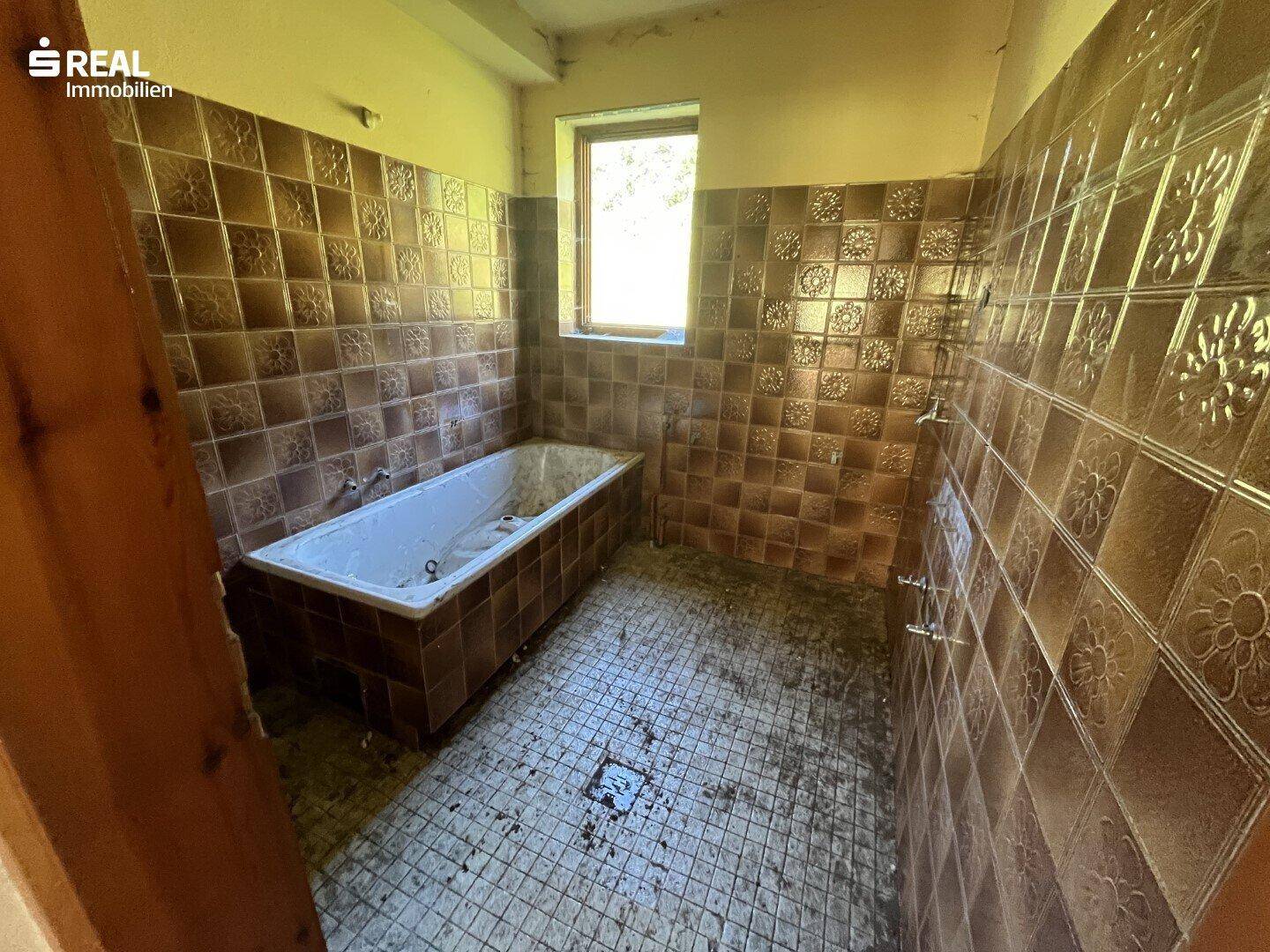 Badezimmer im 80er-Jahre-Stil mit braunen Fliesen, Badewanne und Fenster.