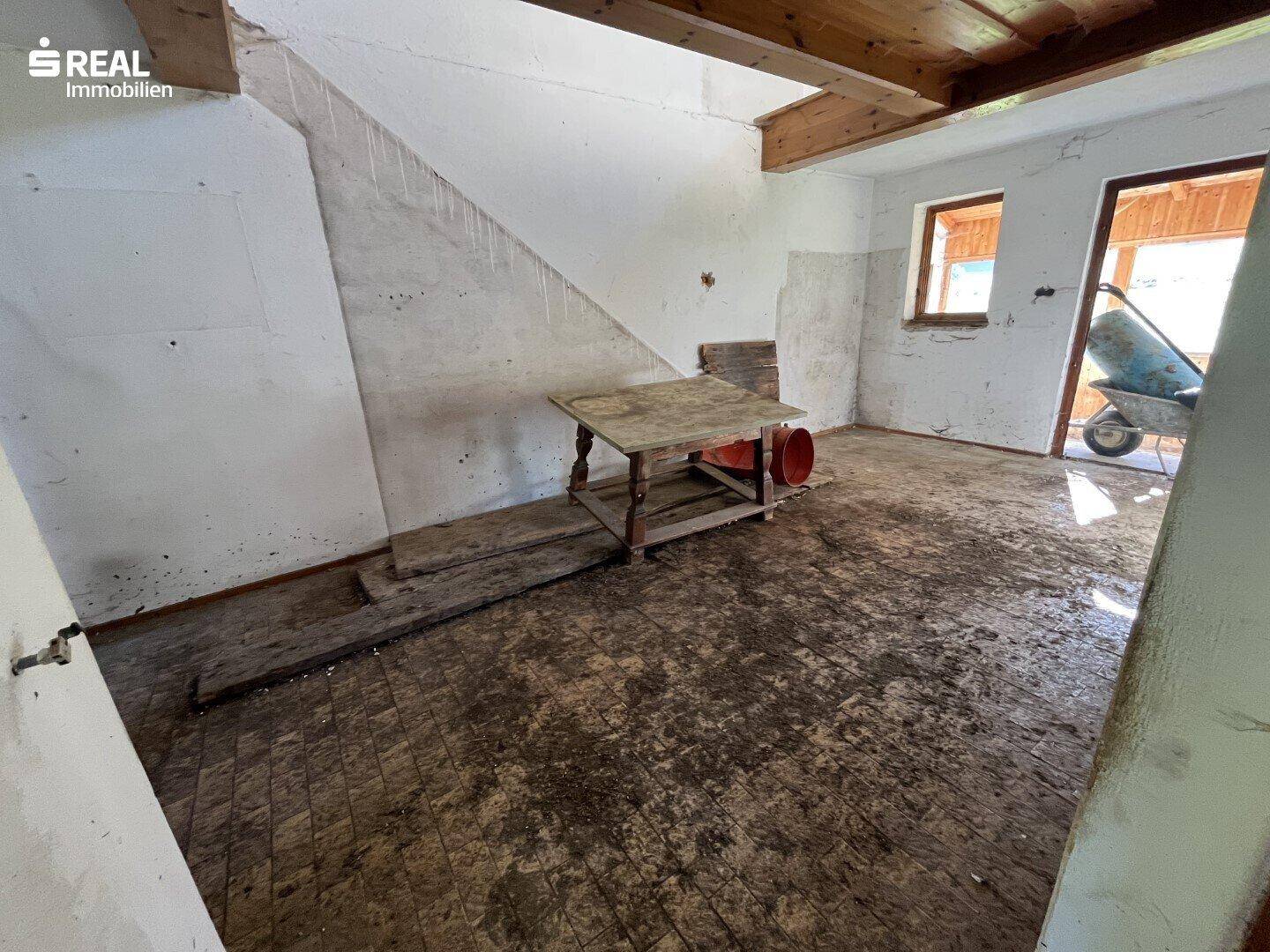 Rustikaler Raum mit Holzbalken, unfertigen Wänden und einem alten Holztisch.