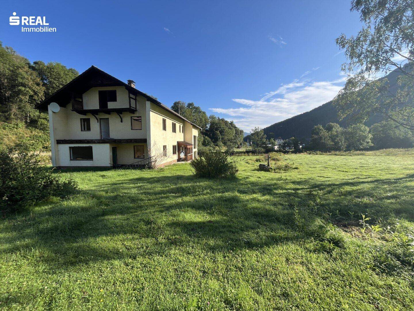 Landhaus in ländlicher Umgebung mit weiten Wiesen und bewaldeten Hügeln.