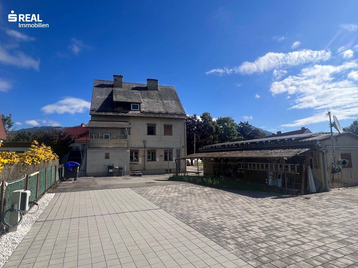 Rückansicht des Gebäudes mit gepflastertem Hof und Nebengebäuden unter blauem Himmel.