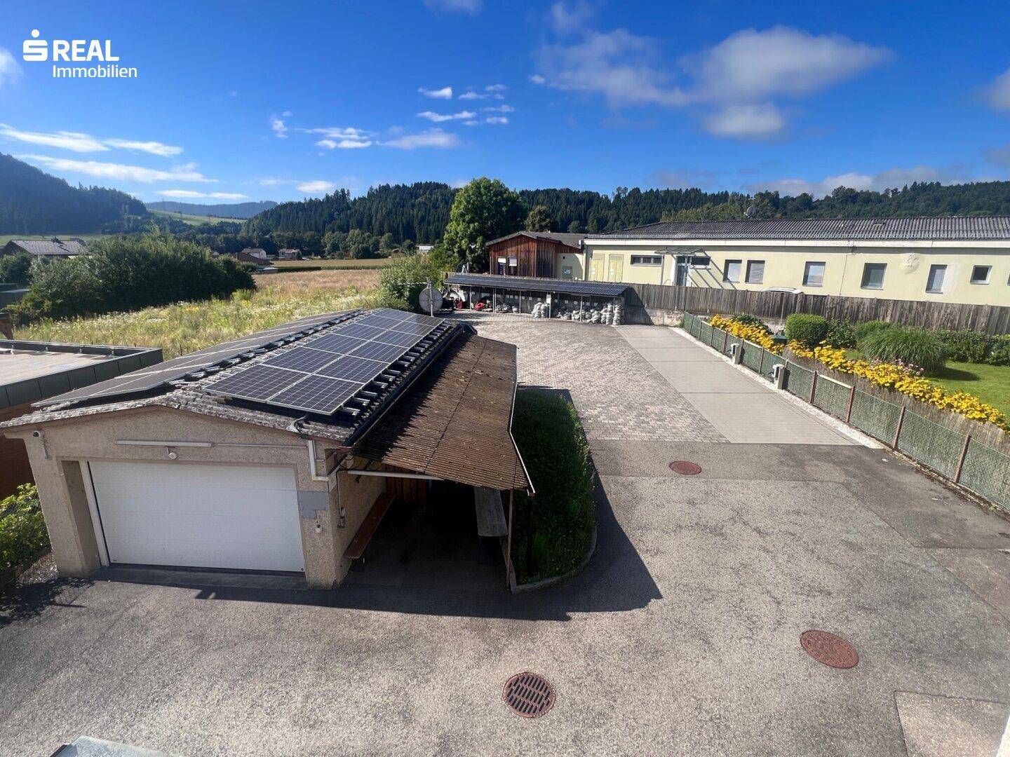 Überblick über den gepflasterten Außenbereich mit Garage, Photovoltaikanlage und angrenzender Natur.