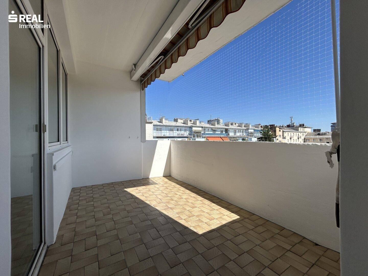 Geräumiger Balkon mit weitem Stadtblick, viel Tageslicht und großen Fenstern zum Innenraum.