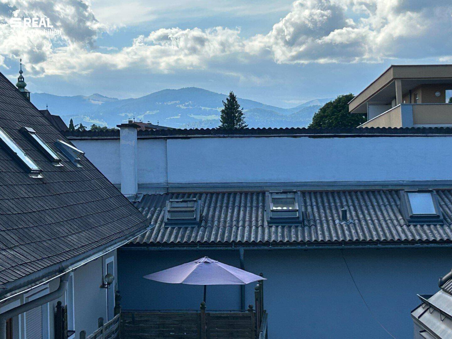 Panoramablick über Dächer auf eine beeindruckende Berglandschaft unter bewölktem Himmel.