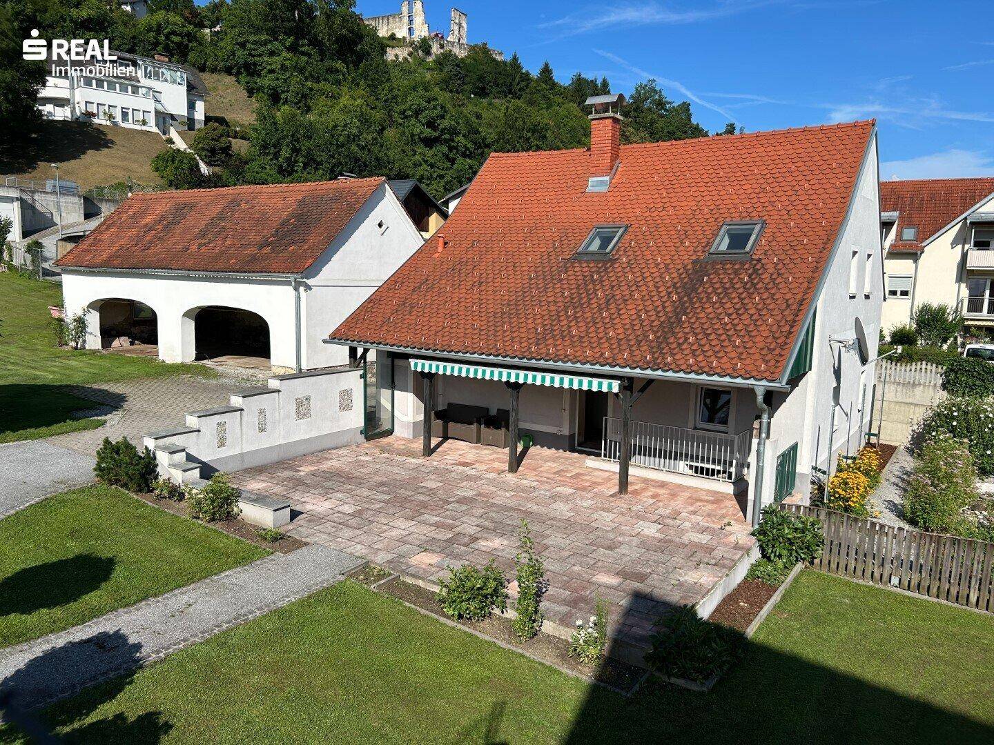 Große gepflasterte Terrasse mit Blick auf ein Nebengebäude und die umliegende Hügellandschaft.