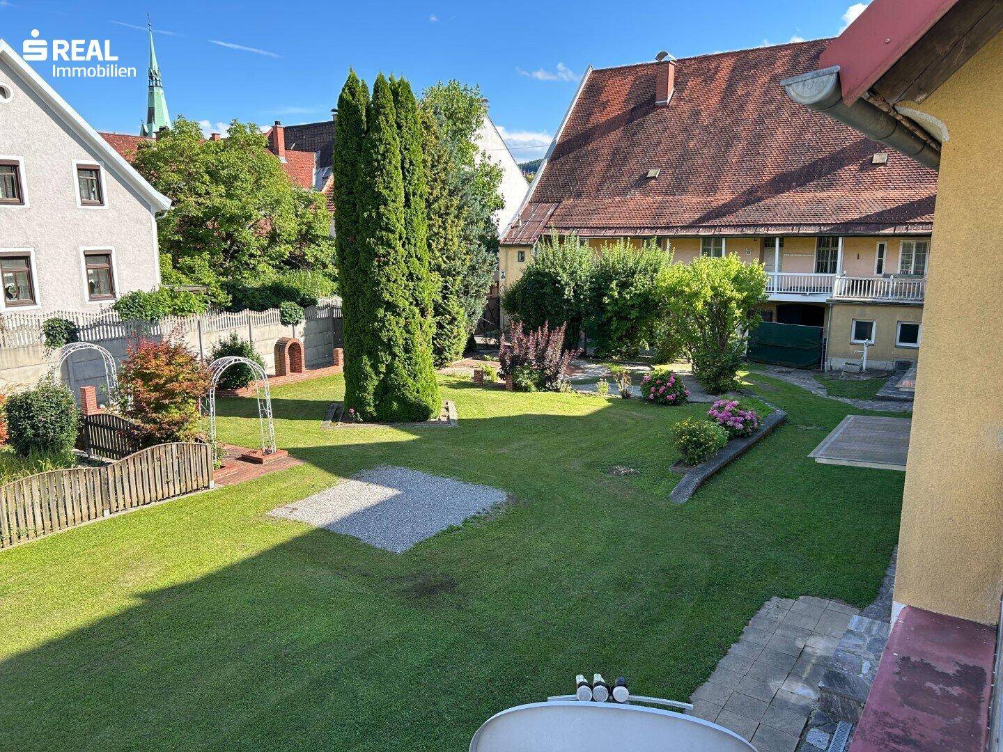Weitläufiger Garten mit gepflegtem Rasen und Blick auf die umliegenden Gebäude und Bäume.
