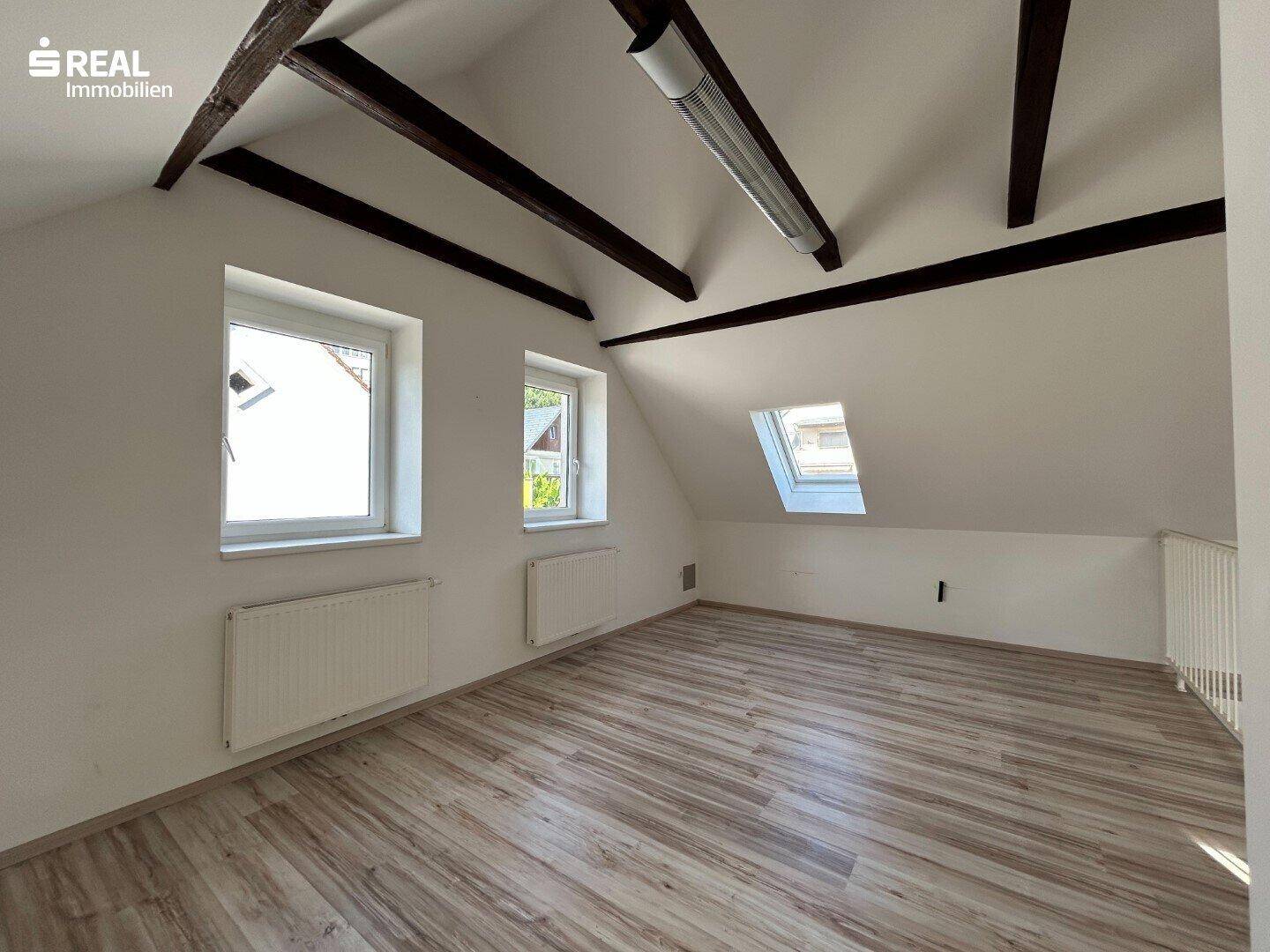 Heller Wohnraum im Dachgeschoss mit sichtbaren Holzbalken, Laminatboden und Dachfenster.