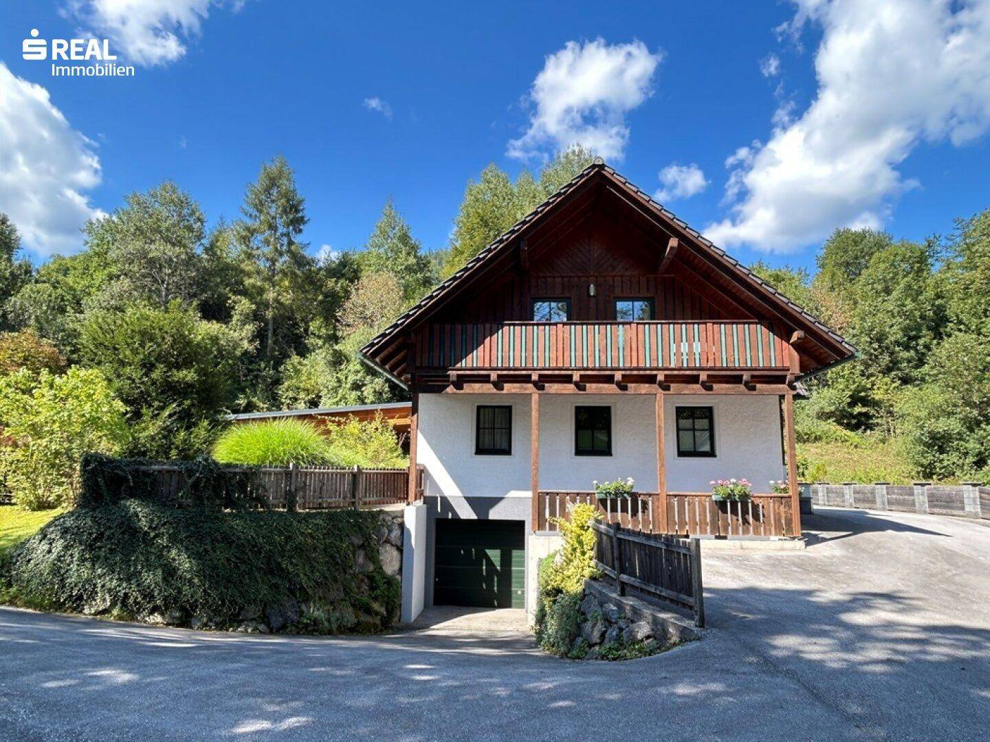 Charmantes Landhaus mit Holzbalkon und integrierter Garage, umgeben von üppiger Natur.