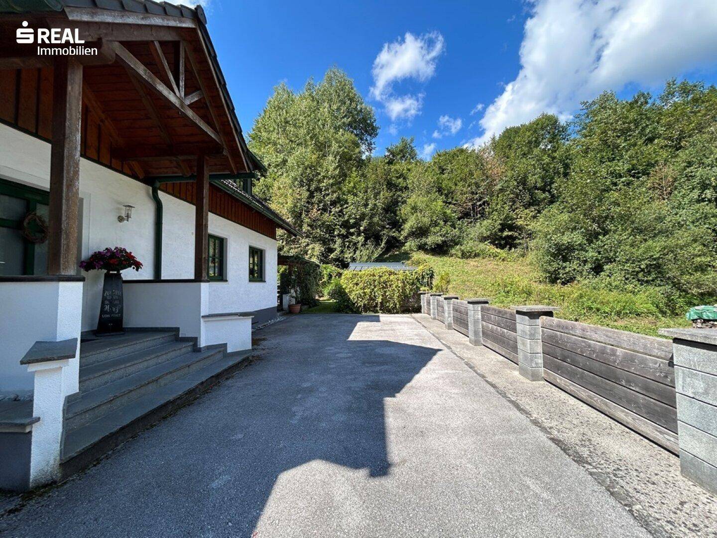 Breite Zufahrt zum Anwesen, gesäumt von einer niedrigen Mauer und üppiger Vegetation.