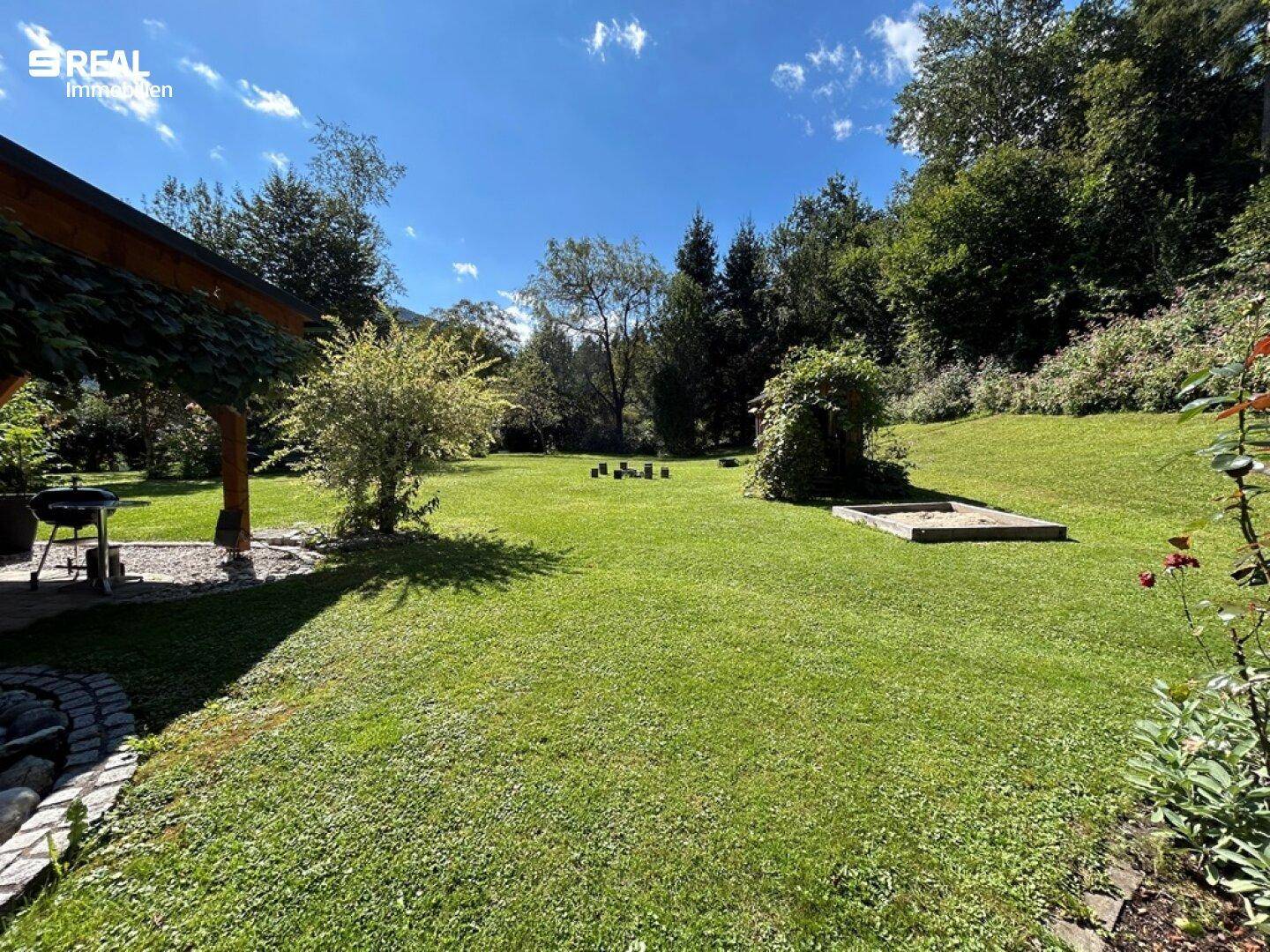 Großer, gepflegter Garten mit Rasenfläche und Sandkasten, ideal für Kinder und Erholung.