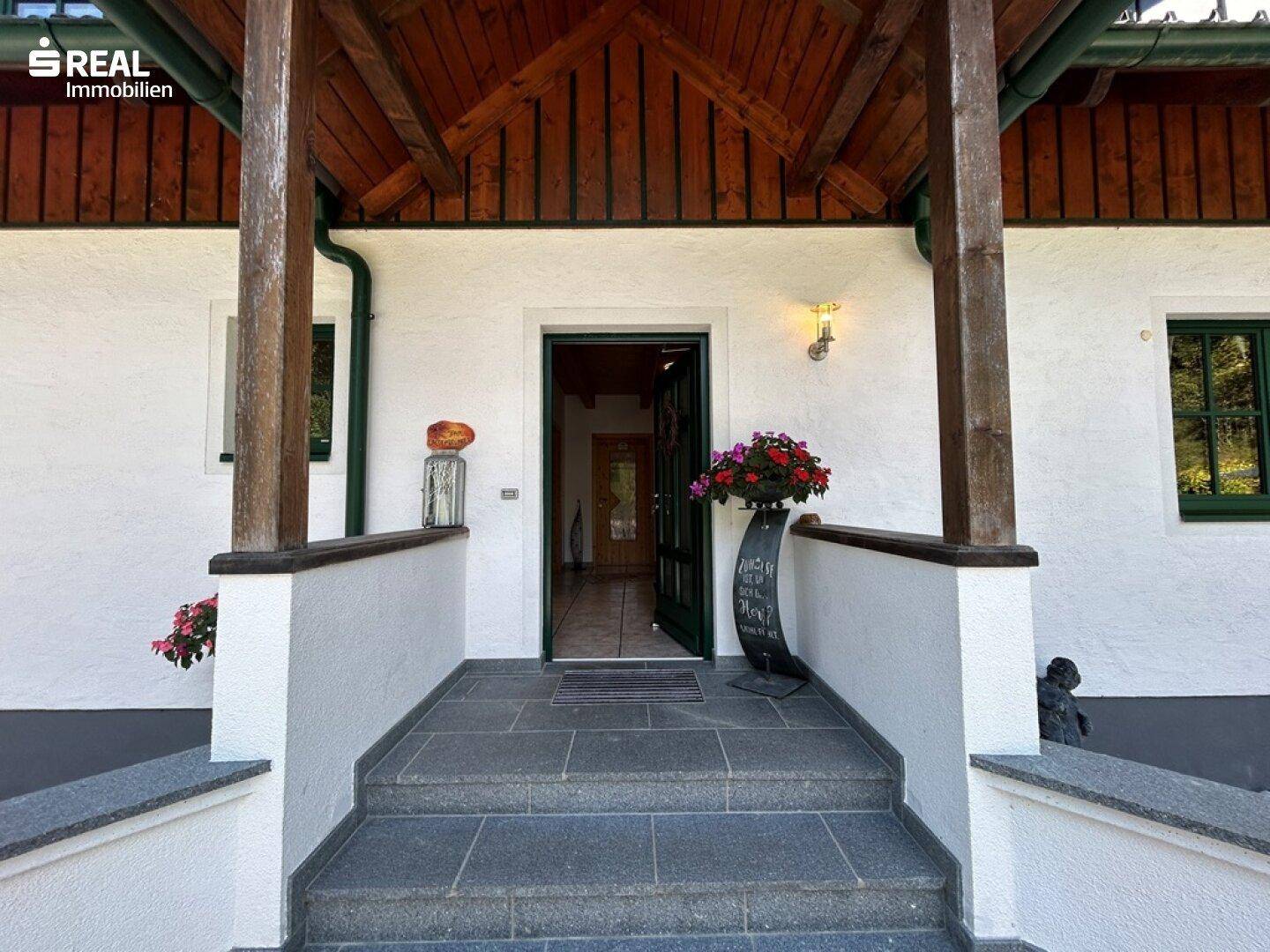 Einladender Hauseingang mit Steinstufen und Blumenarrangements, führt ins Innere des Hauses.