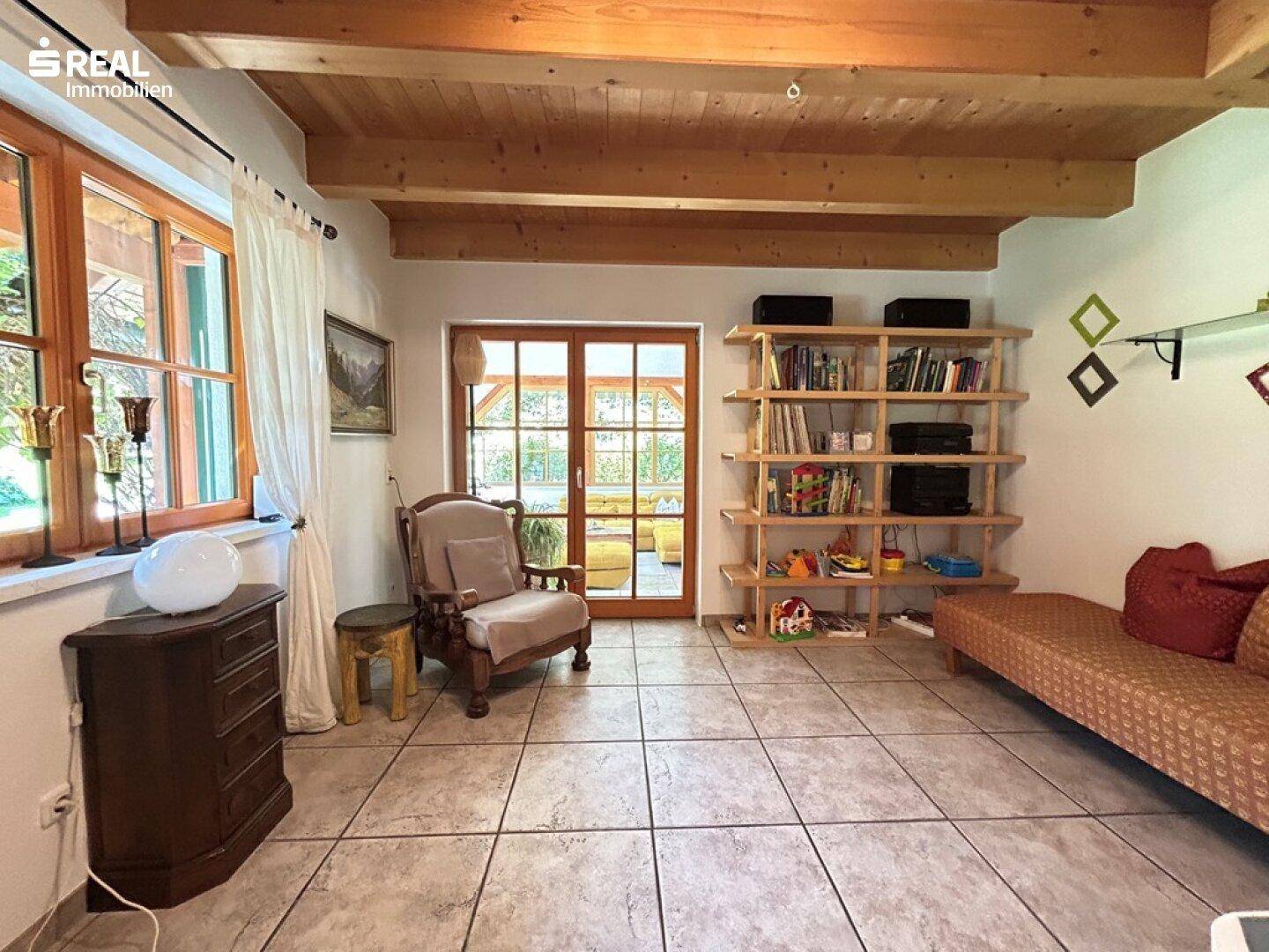 Gemütliches Wohnzimmer mit Fliesenboden, Holzbalkendecke und Bücherregal, hell und einladend.