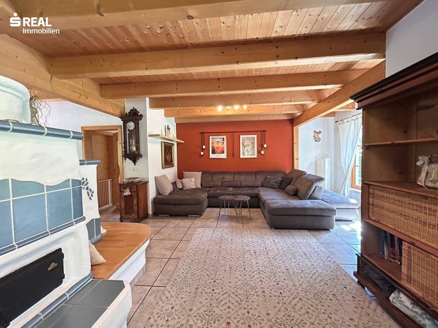 Gemütliches Wohnzimmer mit großem Sofa, Holzbalkendecke und Kachelofen, ideal zum Entspannen.