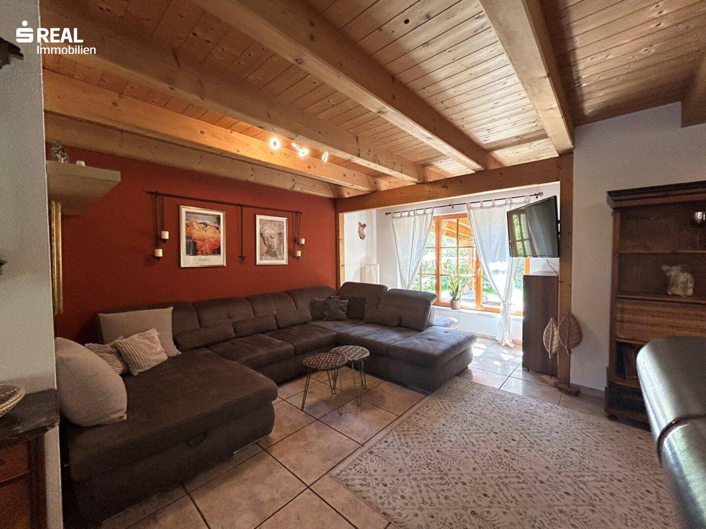 Gemütliches Wohnzimmer mit Holzbalkendecke, roter Akzentwand und großem Ecksofa.