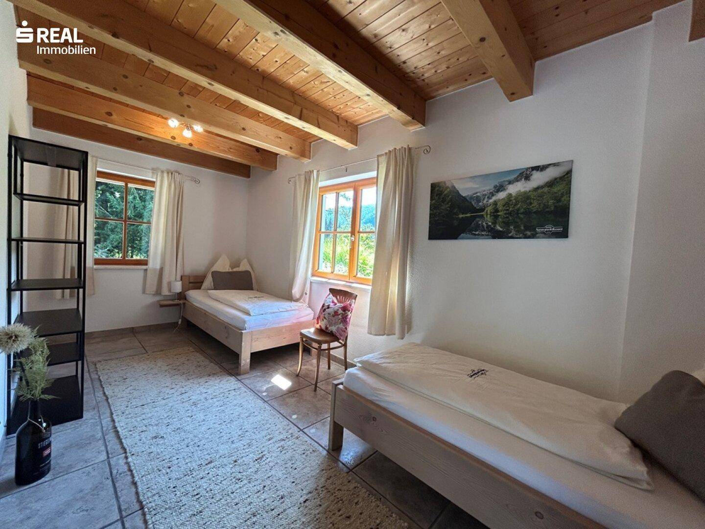 Schlafzimmer mit zwei Einzelbetten, Holzbalkendecke und Blick ins Grüne.