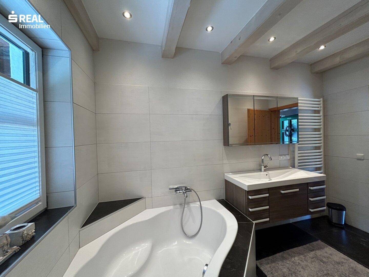 Helles Badezimmer mit Eckbadewanne, Einzelwaschbecken und Spiegelschrank.