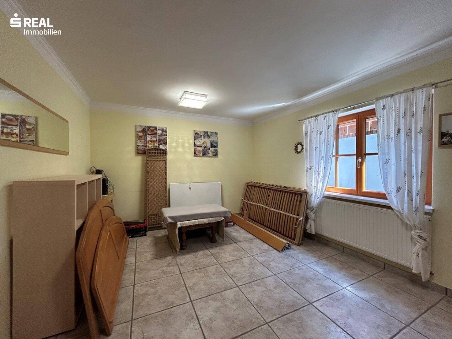 Geräumiges Zimmer mit Fliesenboden, Fenster und gelben Wänden, derzeit als Abstellraum genutzt.