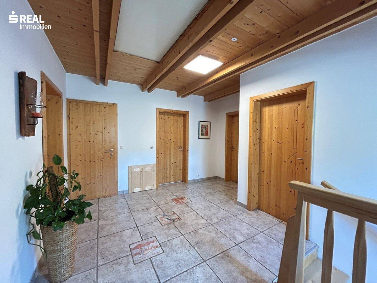 Heller Flur mit Holzbalkendecke, Fliesenboden und mehreren Holztüren.