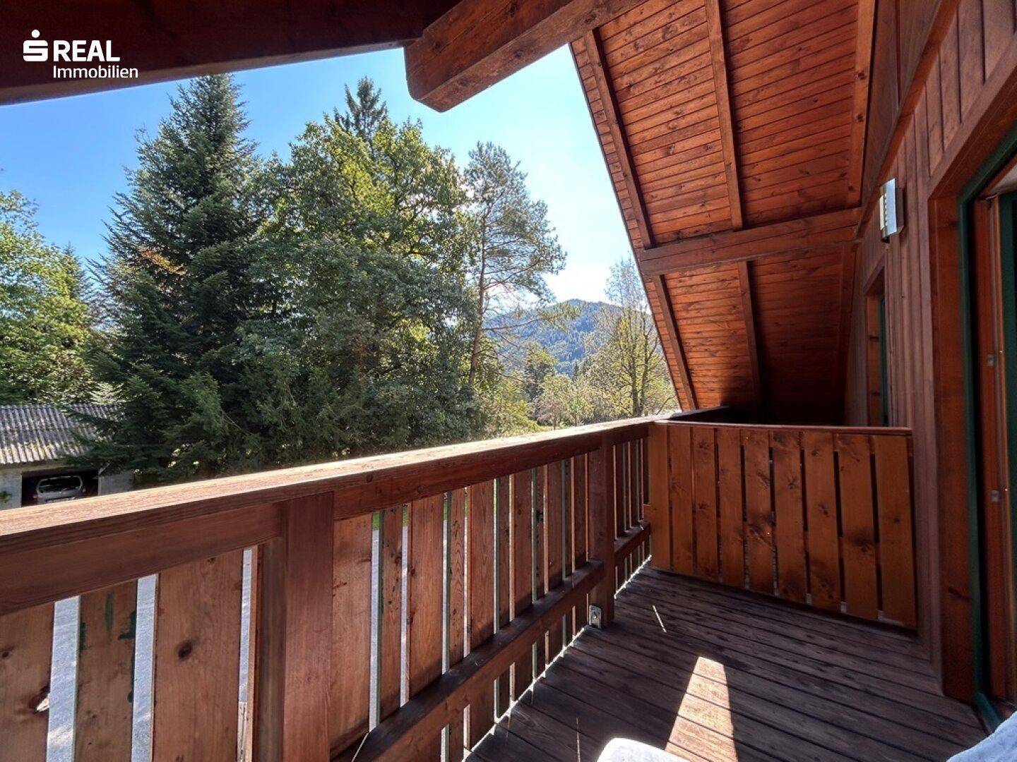 Holzbalkon mit Blick auf grüne Bäume und die umliegende Landschaft.