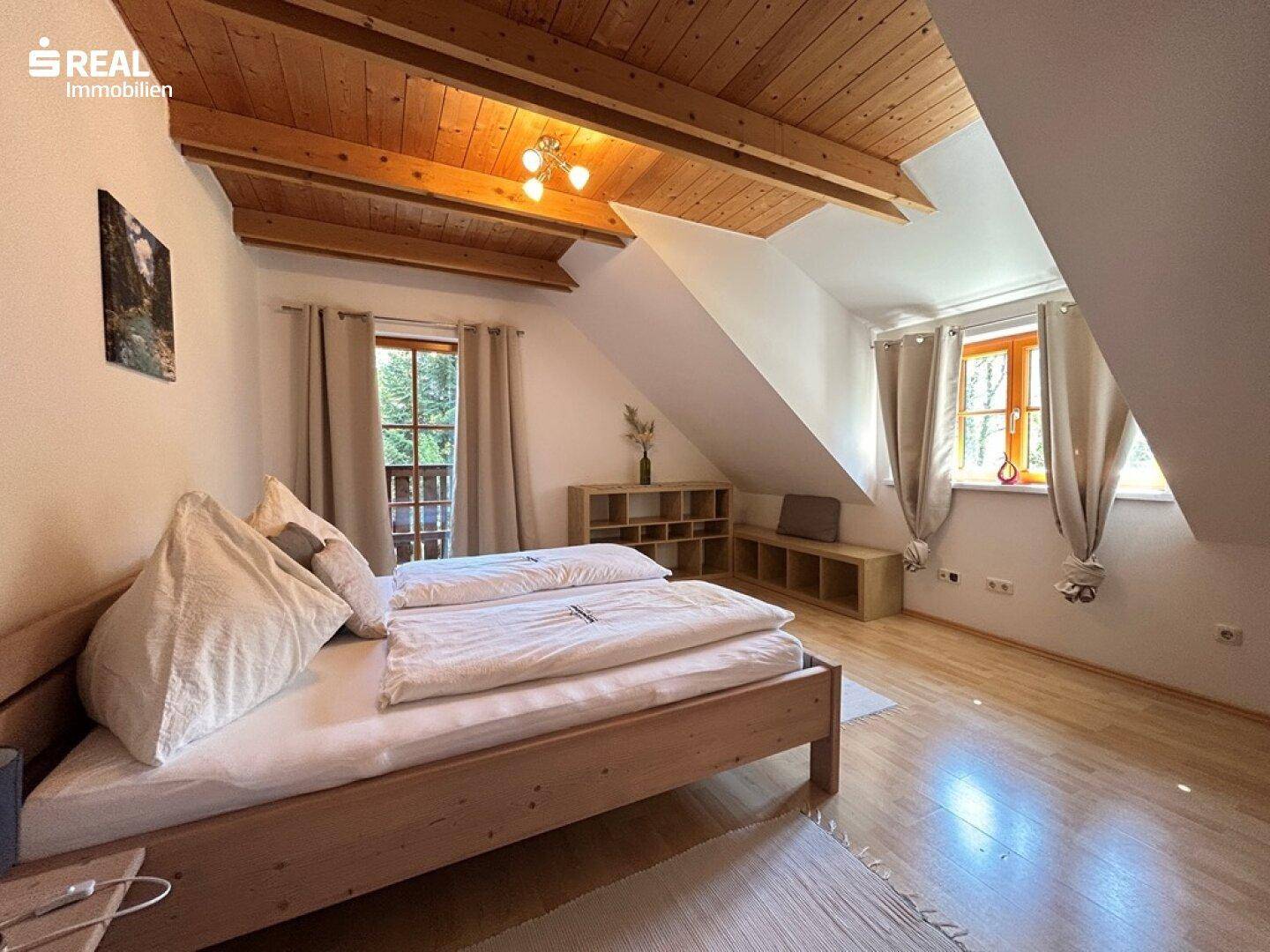 Helles Schlafzimmer im Dachgeschoss mit Holzbalkendecke und schrägen Wänden.
