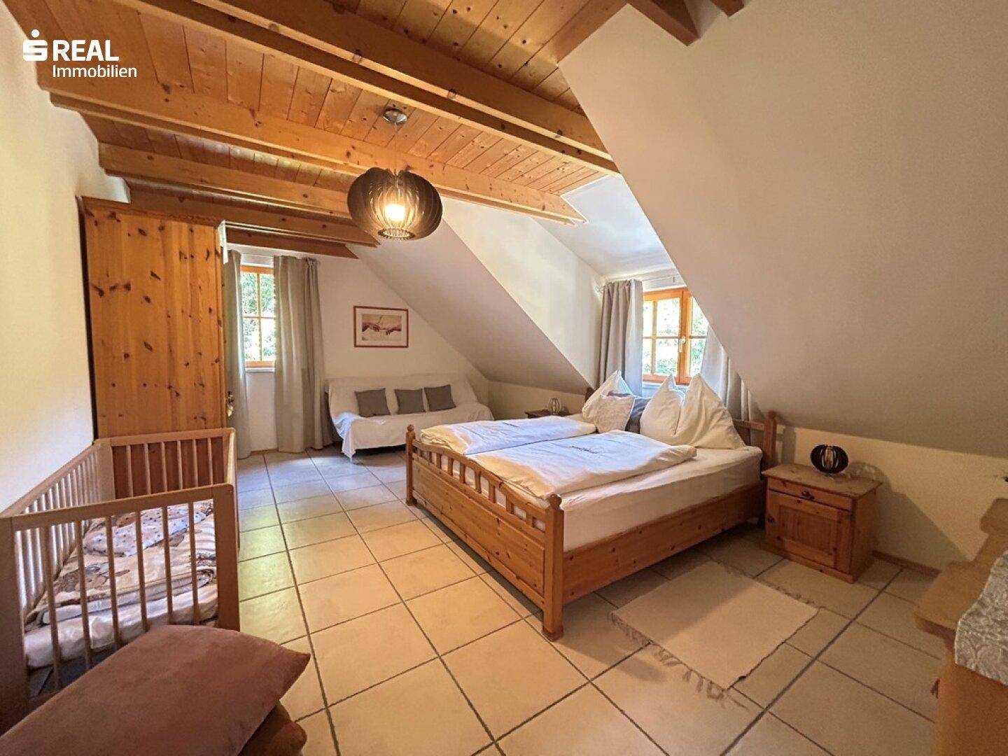Geräumiges Schlafzimmer im Dachgeschoss mit Holzbalkendecke und Kinderbett.