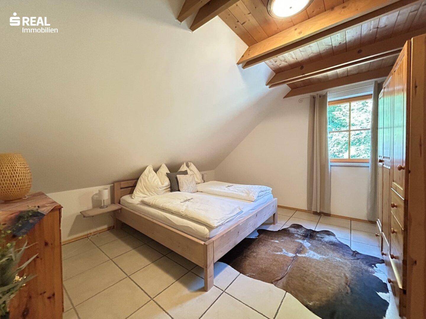 Schlafzimmer im Dachgeschoss mit Holzbalkendecke, Fliesenboden und rustikalem Teppich.