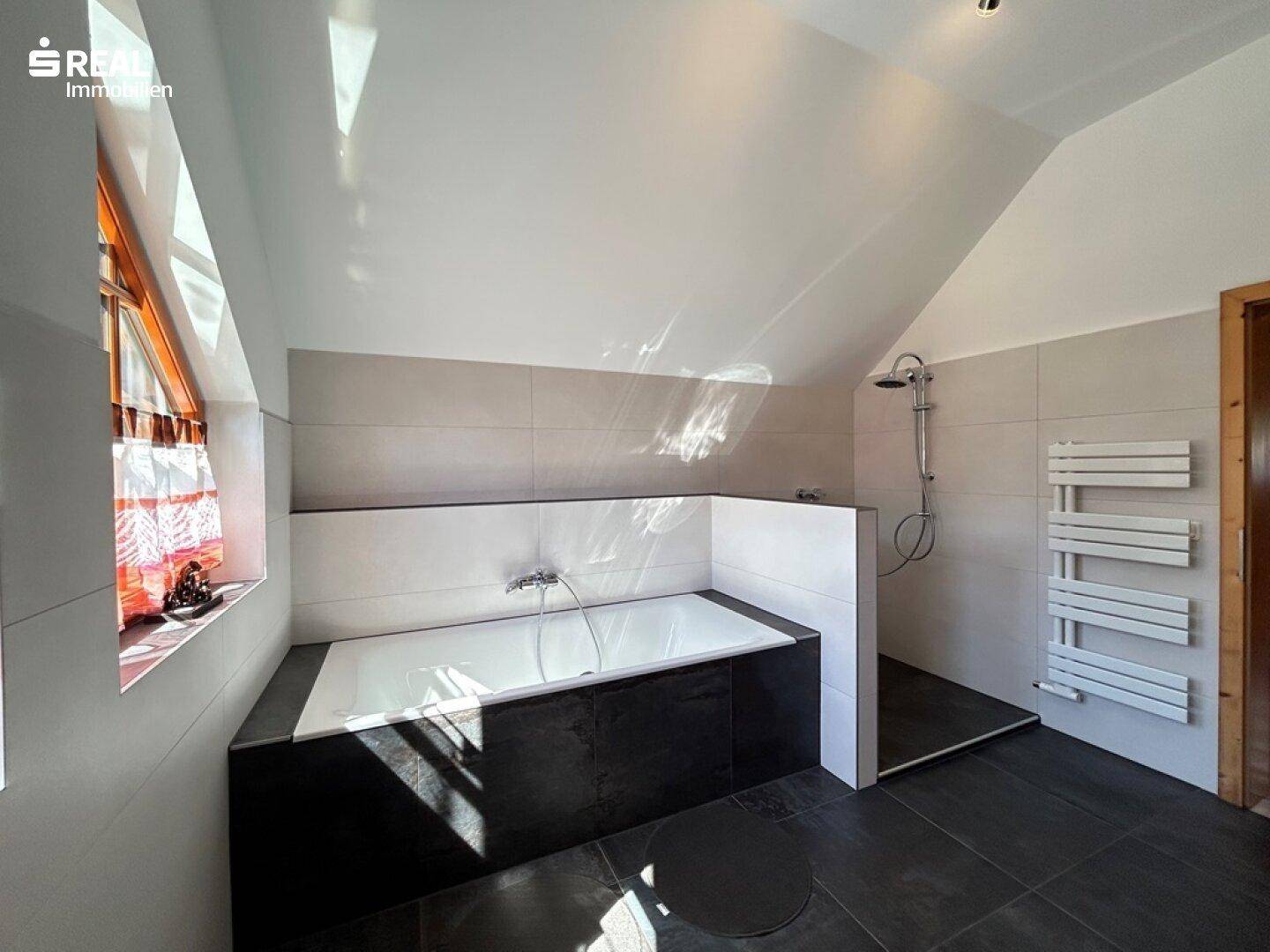 Helles Badezimmer im Dachgeschoss mit Badewanne, Dusche und beheiztem Handtuchhalter.