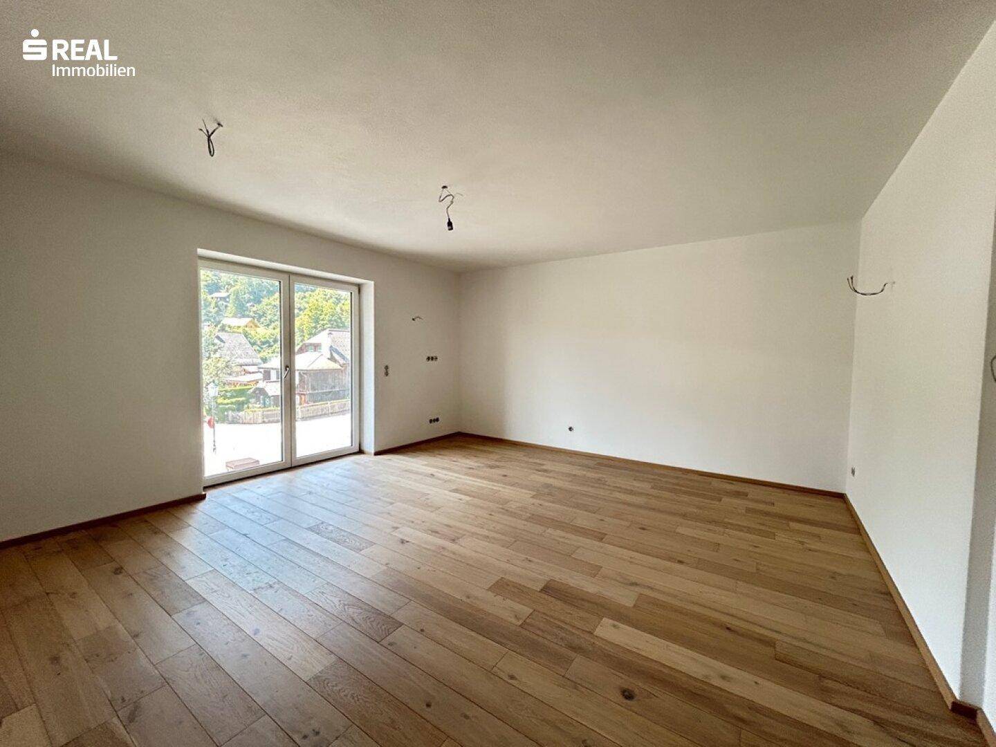 Geräumiges, leeres Zimmer mit Holzboden und großen Glas-Schiebetüren, die Zugang nach draußen bieten.