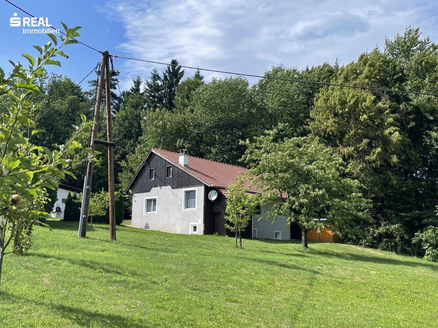 Freistehendes Haus mit Satteldach, umgeben von viel Grün und Bäumen.
