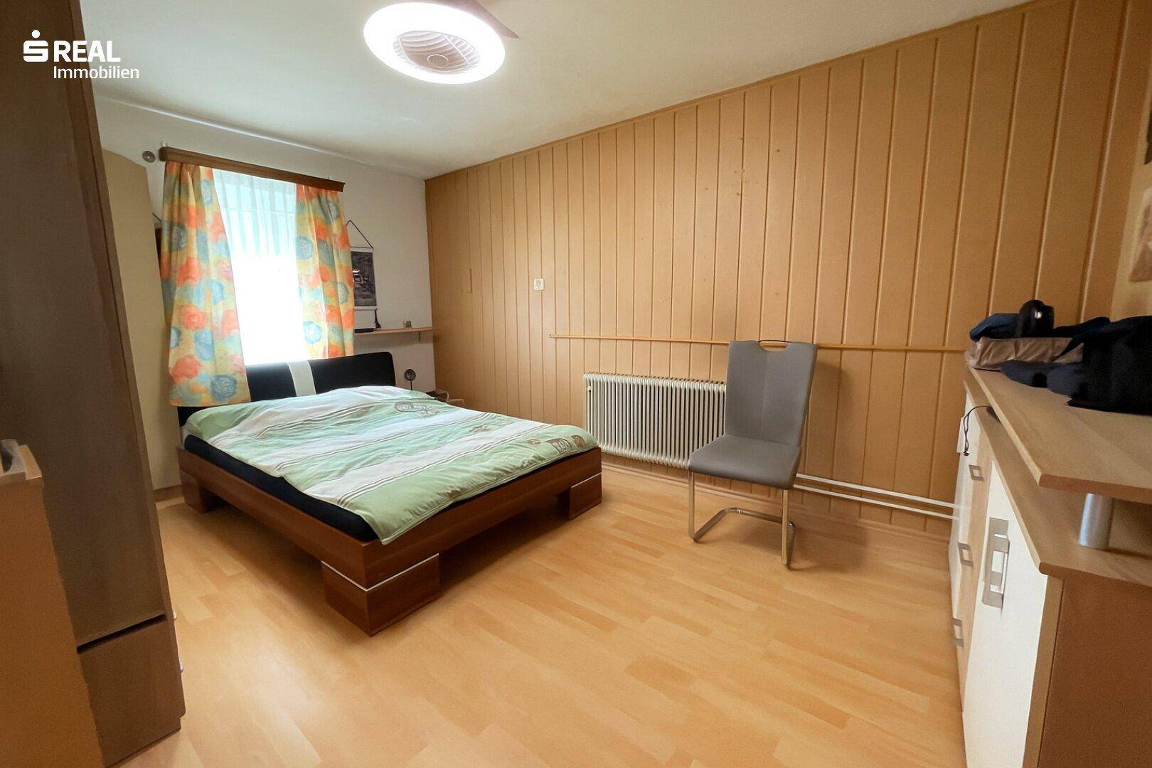 Schlafzimmer mit Holzwänden, Doppelbett und Heizkörper unter dem Fenster.