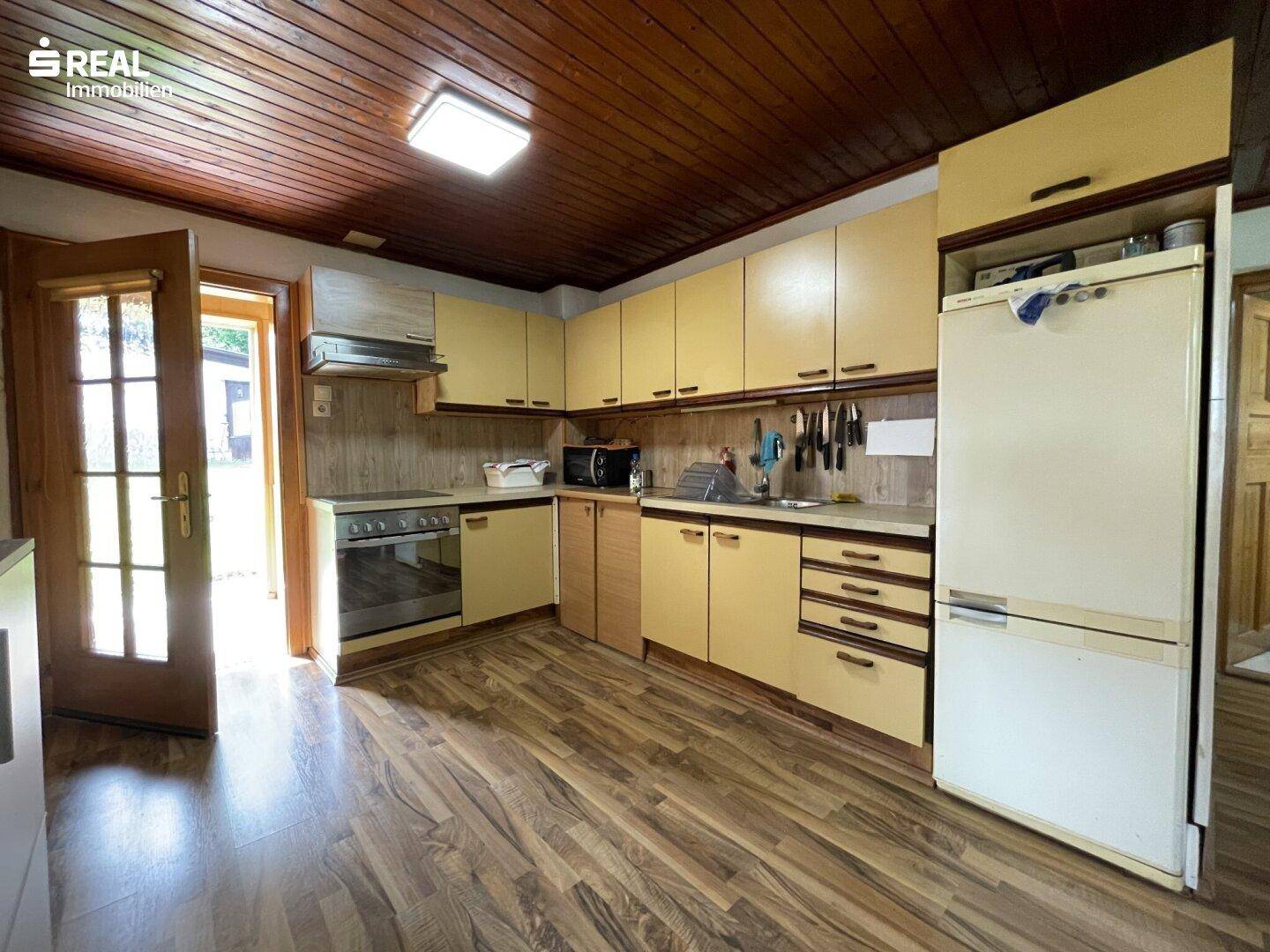 Traditionelle Küche mit Holzdecke, Laminatboden und gelben Einbauschränken.