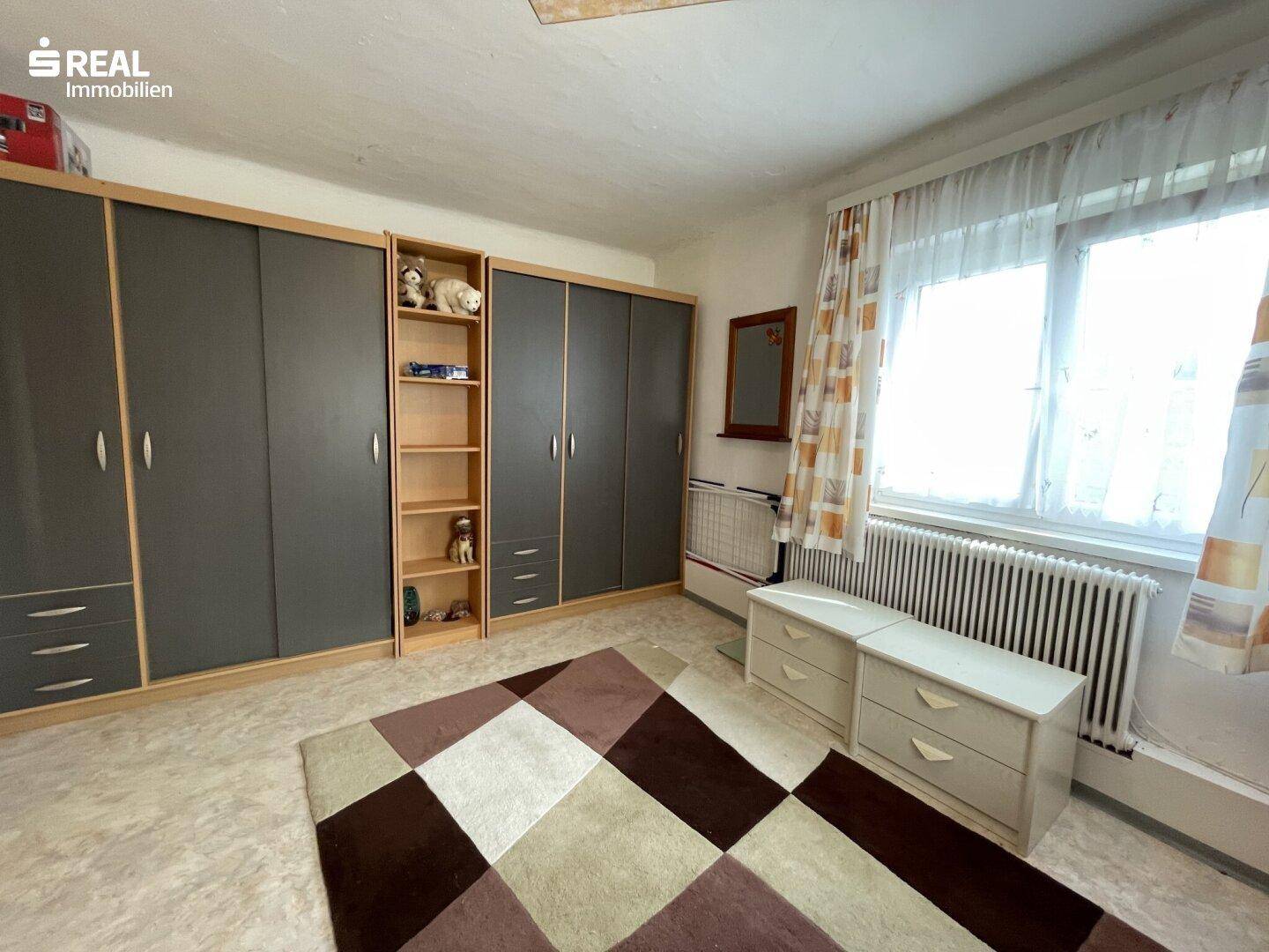 Helles Schlafzimmer mit großem Kleiderschrank, Teppich und Fenster.