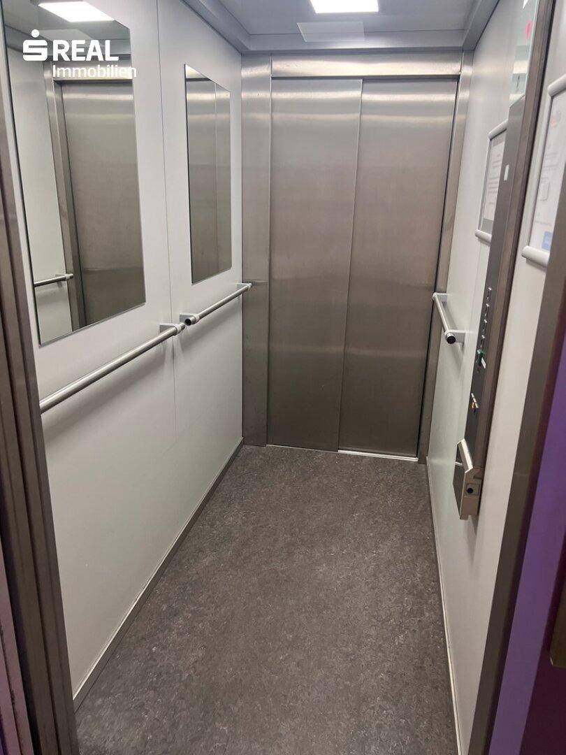 Innenansicht eines modernen Aufzugs mit Edelstahlwänden, Spiegeln und Handläufen.