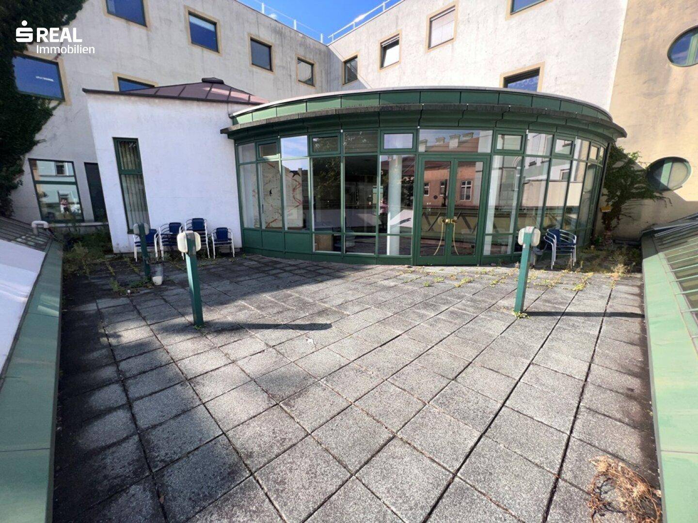 Große gepflasterte Terrasse mit Blick auf ein Gebäude mit runden Glasfenstern.