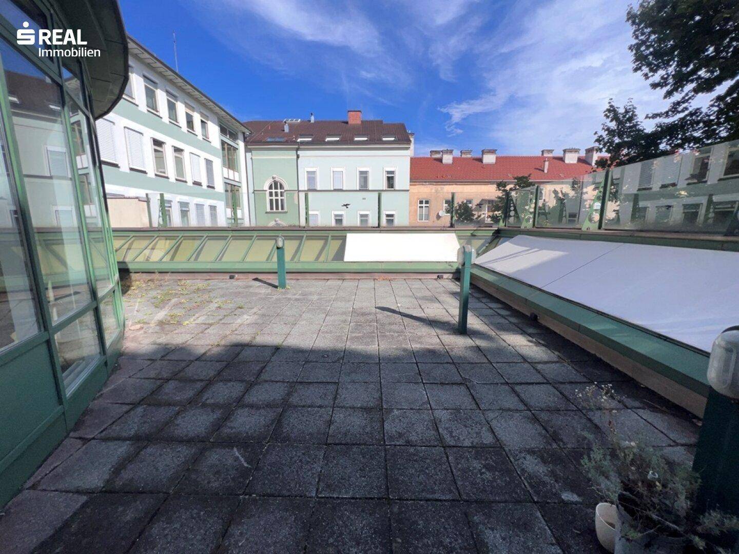 Weitläufige Terrasse mit Pflastersteinen und Blick auf umliegende Gebäude und den Himmel.