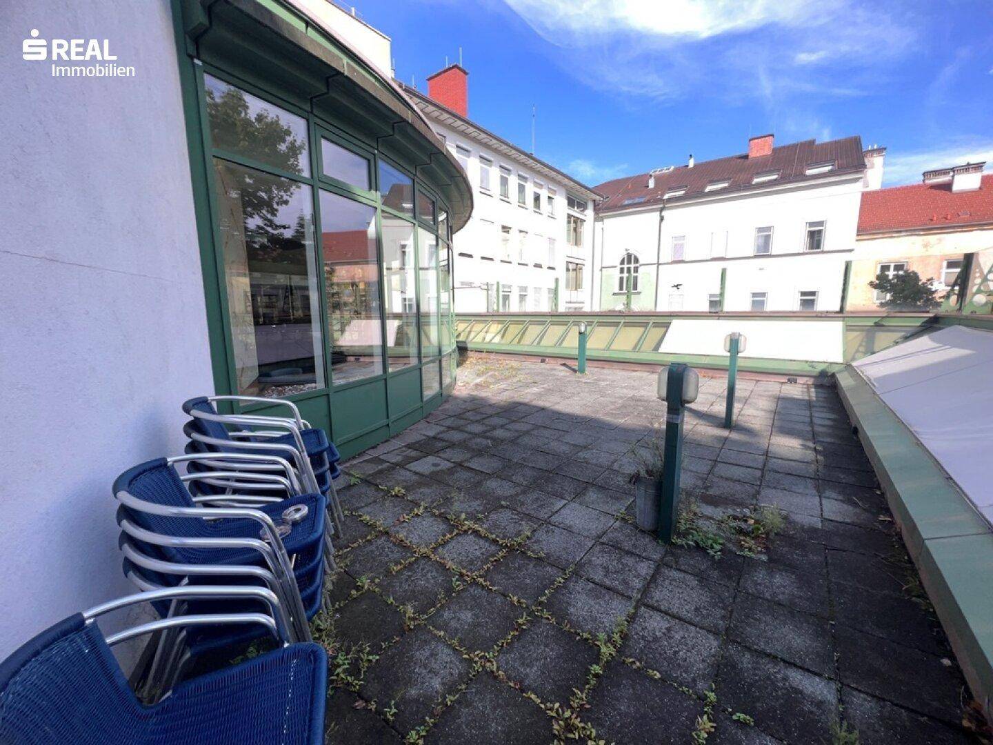 Terrasse mit gestapelten blauen Stühlen und Blick auf die umliegenden Gebäude.