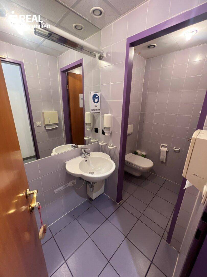 Badezimmer mit lila Fliesen, Waschbecken, Toilette und einem großen Spiegel.