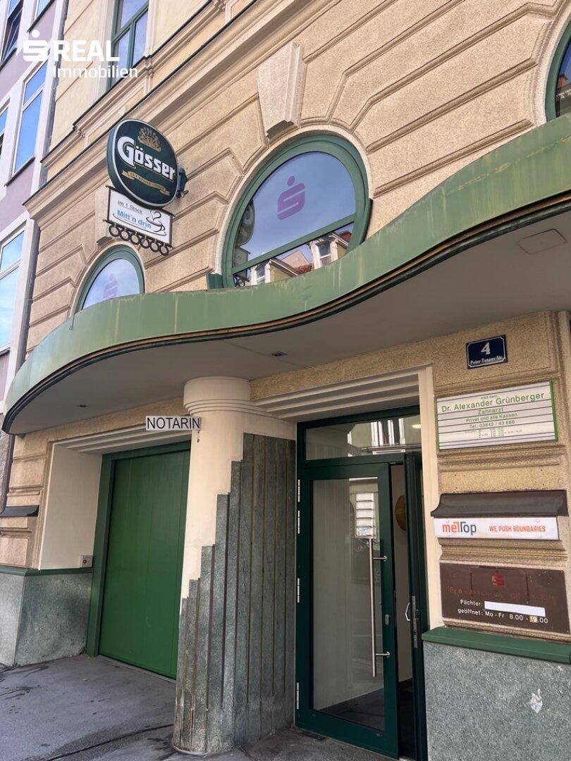 Detailansicht des Eingangs mit grüner Tür, runden Fenstern und Beschilderung.