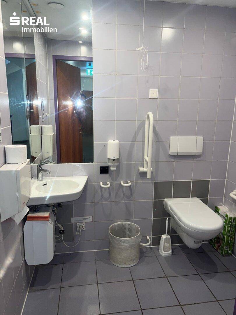 Barrierefreier Toilettenraum mit Haltegriffen, wandhängendem WC und Waschbecken.