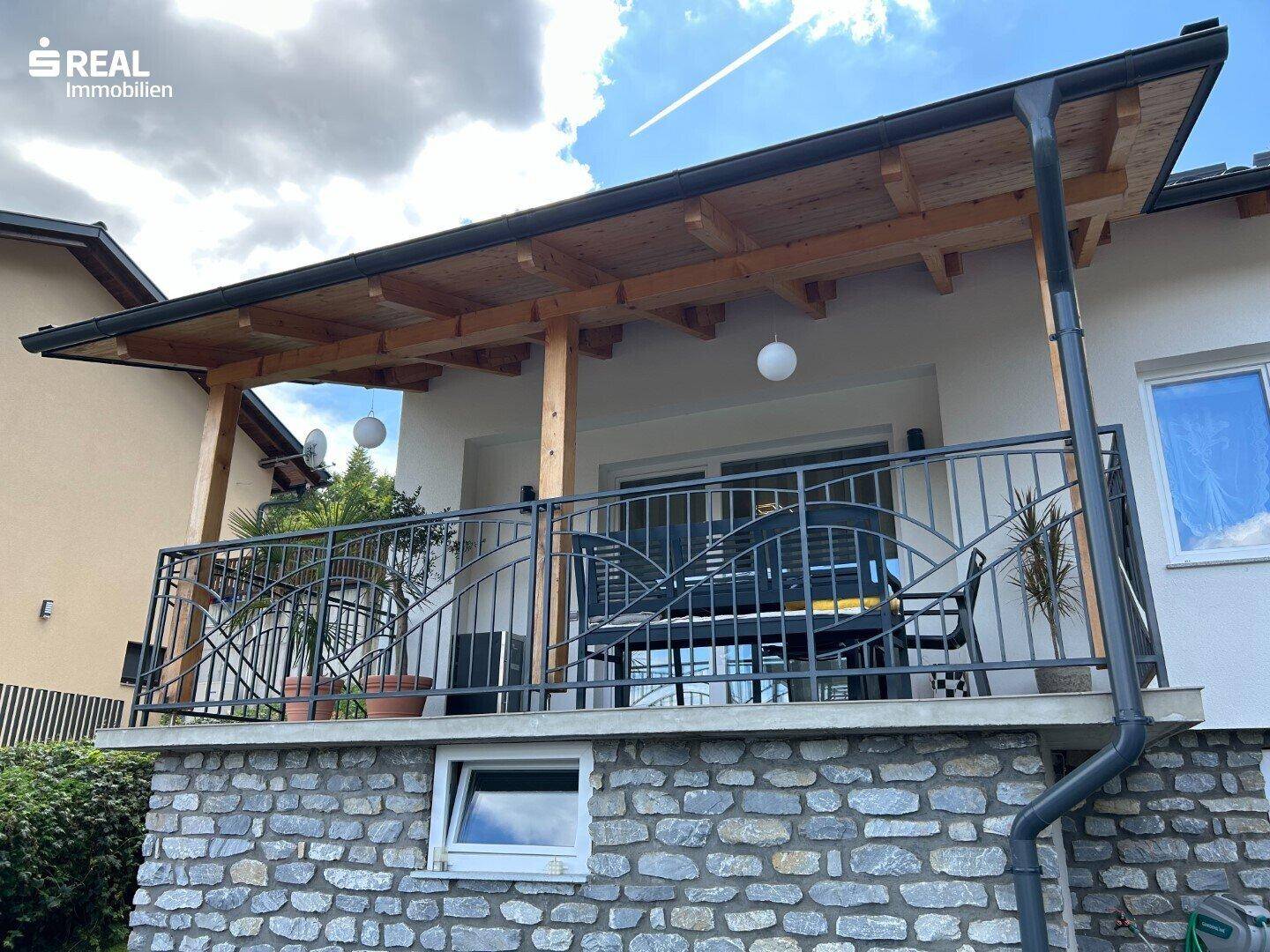 Überdachter Balkon mit schmiedeeisernem Geländer und Steinverkleidung an der Fassade.