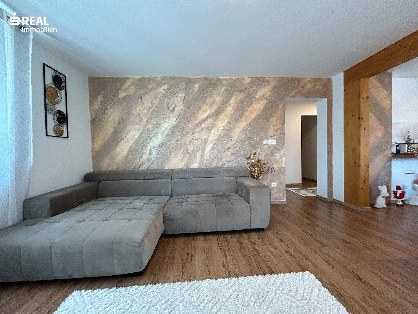 Gemütliches Wohnzimmer mit großem Ecksofa, Holzboden und einer strukturierten Akzentwand.